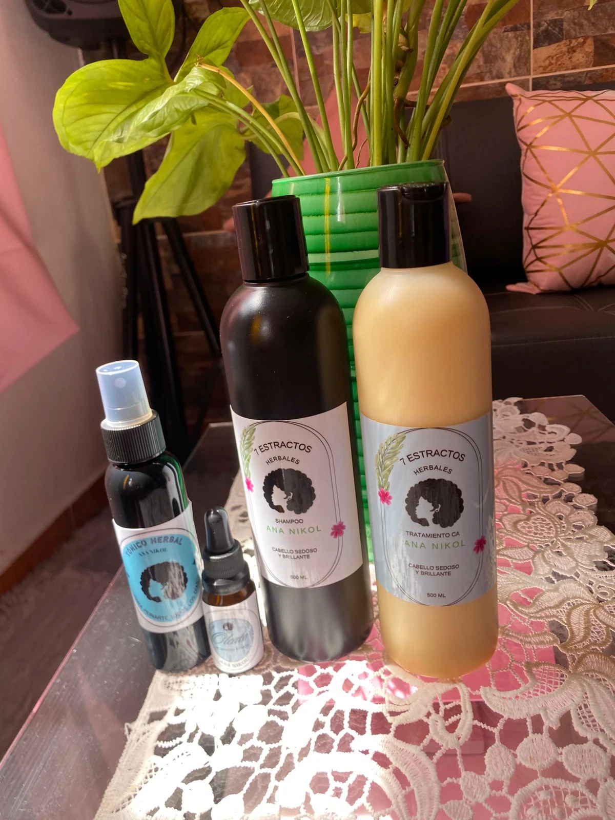 Kit capilar Ana Nikol con shampoo, tratamiento y tónico herbal, presentado en botellas sobre mesa decorada.