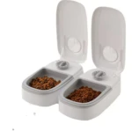 Dos dispensadores automáticos de comida para mascotas de plástico blanco con tapas abiertas y recipientes llenos de croquetas.