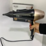 Secador de pelo Nube Keratin Therapy negro y dorado de 3000W sostenido por una mano.