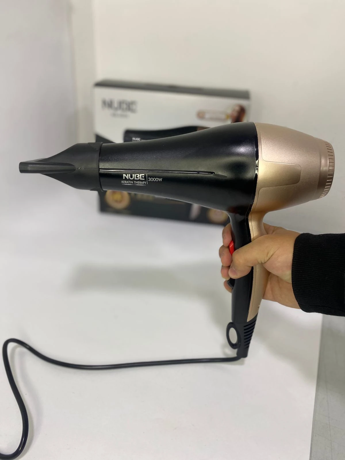 Secador de pelo Nube Keratin Therapy negro y dorado de 3000W sostenido por una mano.