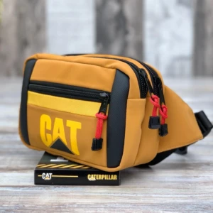 Canguro Caterpillar color mostaza con logo amarillo, dos cierres con cordón rojo, sobre caja de presentación.