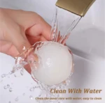 Quita pelusas lavable esférico blanco enjuagándose bajo un grifo dorado, agua salpicando, fácil de limpiar.