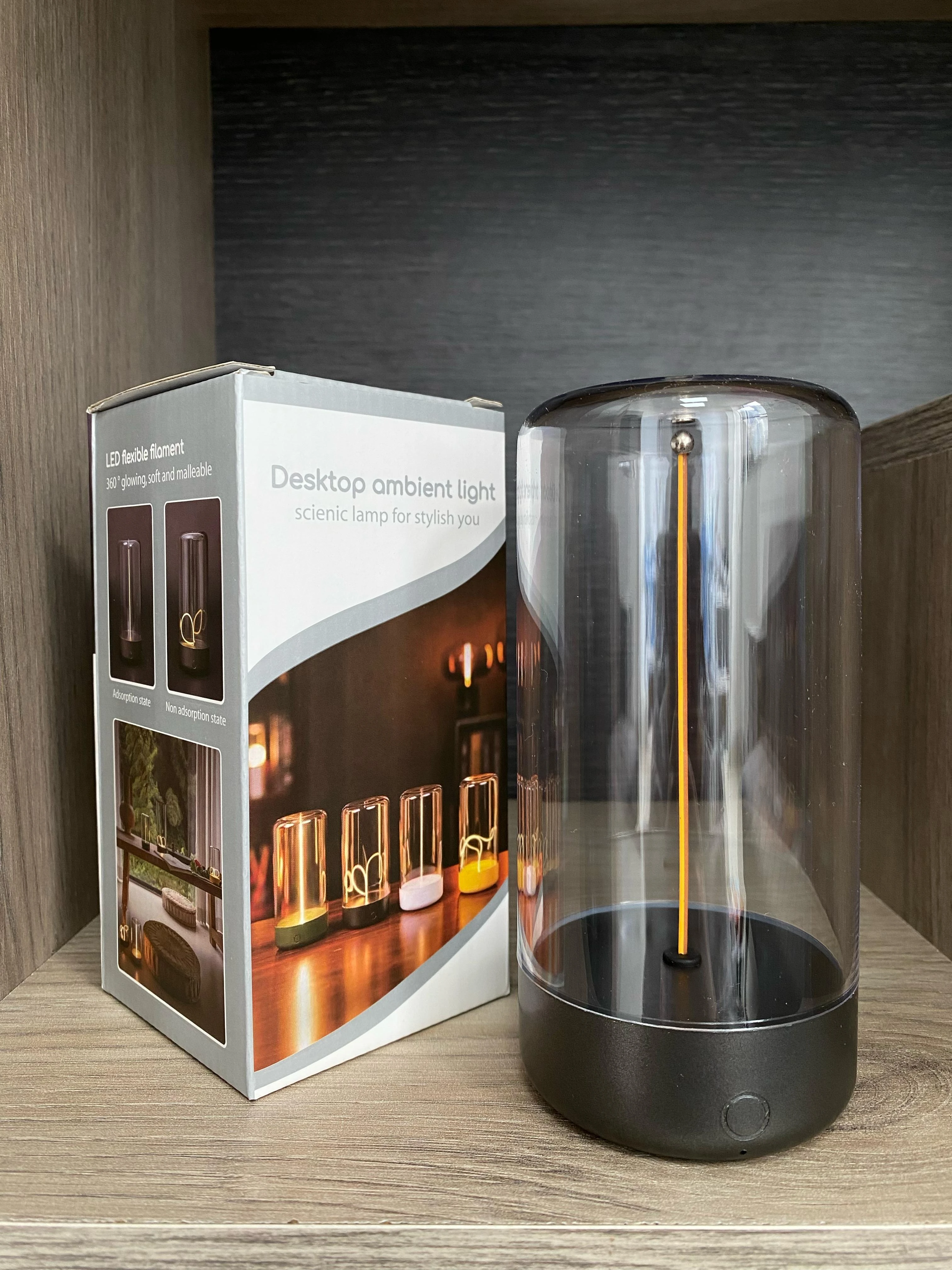 Lámpara táctil imantada de escritorio con filamento LED flexible, junto a su caja de empaque donde se muestra el diseño con base negra y domo transparente.