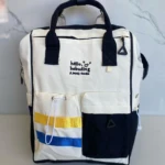 Pañalera blanca con negro, dos bolsillos frontales, uno con rayas amarillas y azules.