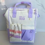 Pañalera blanca y lila con bordado "hello babuding", dos bolsillos frontales con diseño de rayas y cordones.