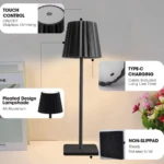 Lámpara LED elegante de aluminio negro con pantalla plisada, control táctil, puerto de carga tipo C y base con antideslizante para mayor estabilidad.