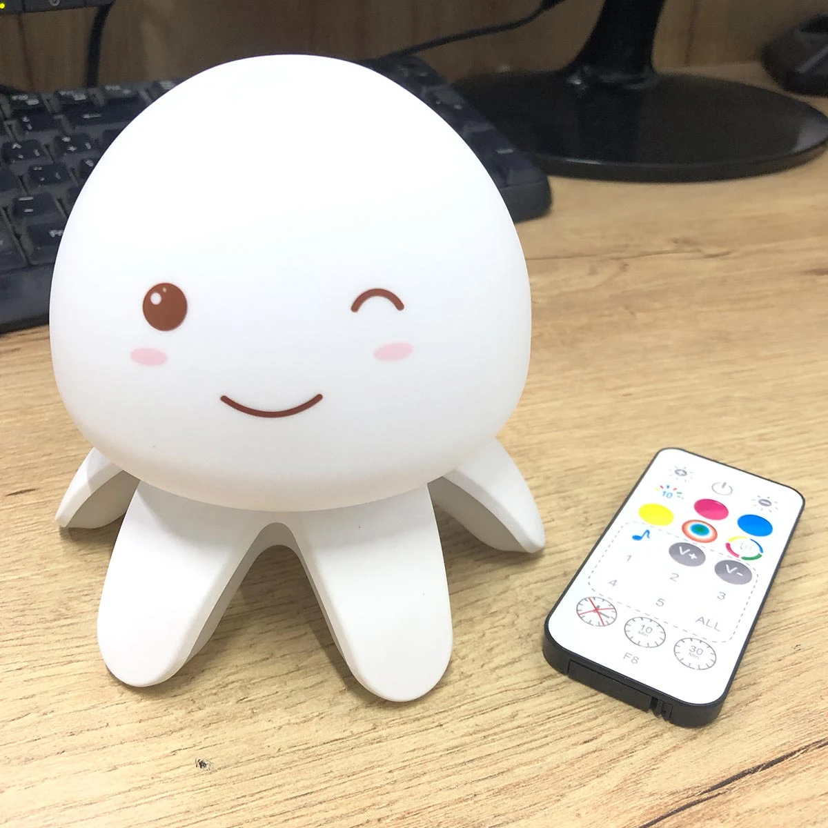 Lámpara infantil de ruido blanco forma de medusa blanca con expresión feliz, acompañada de control remoto multifuncional sobre una mesa de madera.