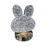 Lámpara LED de mesa con figura de conejo en acrílico facetado, base cilíndrica metálica cromada.
