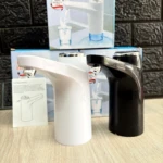 Dispensador eléctrico de agua automático, modelos blanco y negro, sobre superficie de madera clara y fondo de ladrillo oscuro.