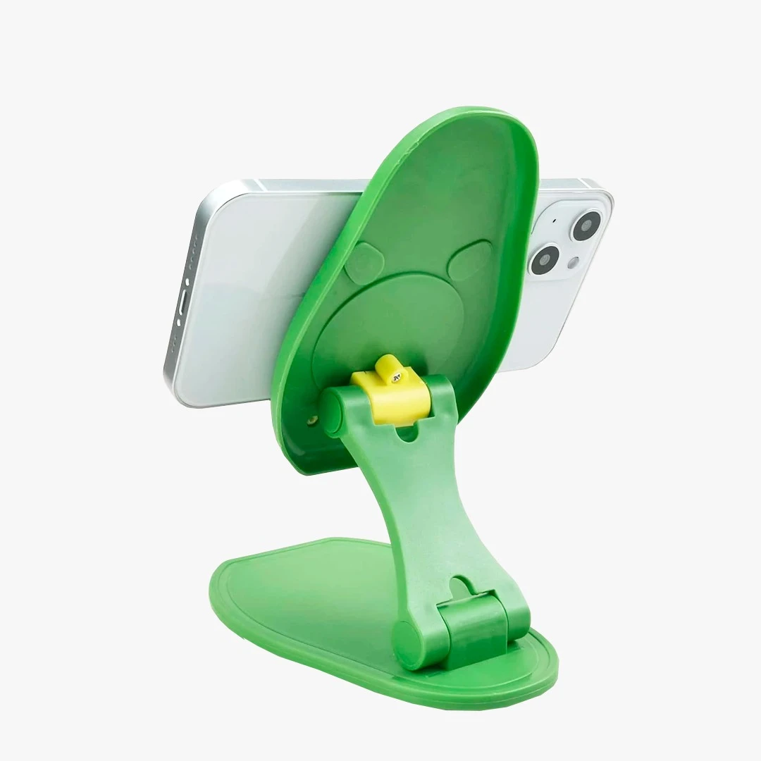 Soporte plegable verde con forma de aguacate sosteniendo un celular plateado, ideal para escritorio.