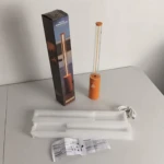 Mini lámpara de ambiente minimalista color naranja, incluye caja, cable de carga USB, empaque protector y manual de usuario sobre una mesa blanca.