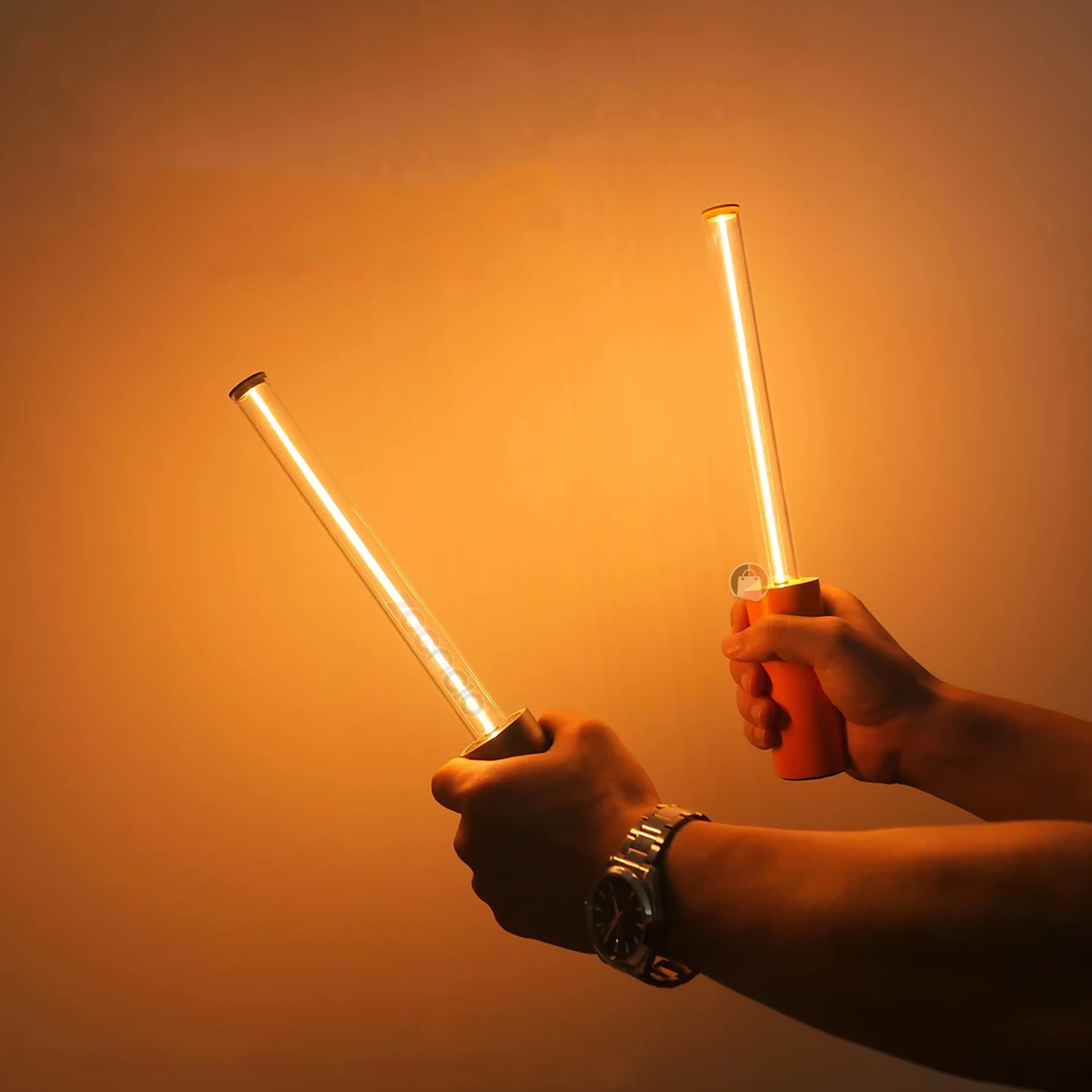 Manos sostienen dos mini lámparas minimalistas de ambiente con luz LED cálida, diseño cilíndrico traslúcido, mango naranja y acabado en metal plateado.