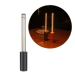 Mini lámpara de ambiente minimalista con base cilíndrica negra y tubo de luz LED vertical cálida, incluye vista de uso sobre mesa en tonos negro y naranja.