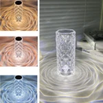 Lámpara de mesa cristal facetado, proyectando patrones de luz anillados en blanco cálido, ámbar y azul.