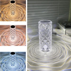 Lámpara de mesa cristal facetado, proyectando patrones de luz anillados en blanco cálido, ámbar y azul.