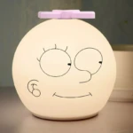 Lámpara nocturna de silicona blanca con rostro caricaturesco y ventilador rosa en la parte superior.