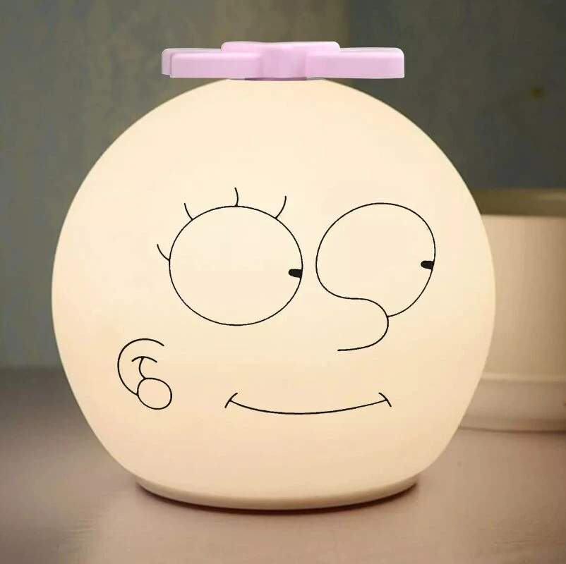 Lámpara nocturna de silicona blanca con rostro caricaturesco y ventilador rosa en la parte superior.