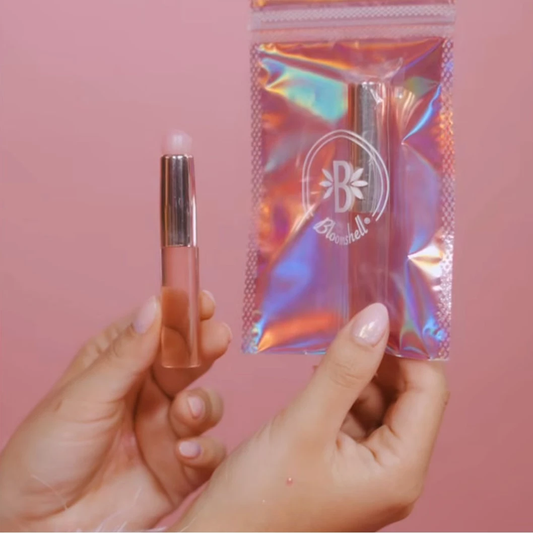 Brocha siliconada para labios color rosa pálido, dentro de empaque holográfico iridiscente marca Bloomshell.