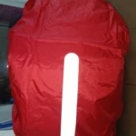 Forro impermeable rojo para morral con franja reflectiva vertical, ideal para protegerlo de la lluvia.