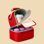 Pañalera térmica roja abierta con recipientes de comida y termo rosado en su interior.