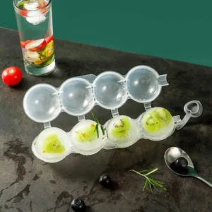 Molde redondo para 3 bolas de hielo transparente con kiwi en su interior, al lado de un vaso con frutas y una cuchara con arándanos.