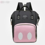 Morral pañalera negro con bolsillo frontal rosa con diseño de dos círculos blancos, tipo orejas de personaje.