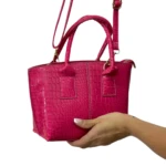 Bolso dama fucsia metalizado con textura de cocodrilo, asa corta y correa ajustable, sostenido por mano.