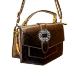 Bolso pequeño marrón cobrizo efecto charol arrugado, con solapa y broche cuadrado pedrería brillante, asa superior y correa.