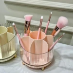 Organizador de cosméticos rosa con compartimentos y brochas de maquillaje, base transparente con patas doradas.