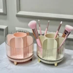 Organizador de brochas de maquillaje rosa y crema con compartimentos, patas doradas y acabado acanalado en cristal.