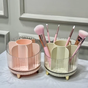 Organizador de brochas de maquillaje rosa y crema con compartimentos, patas doradas y acabado acanalado en cristal.