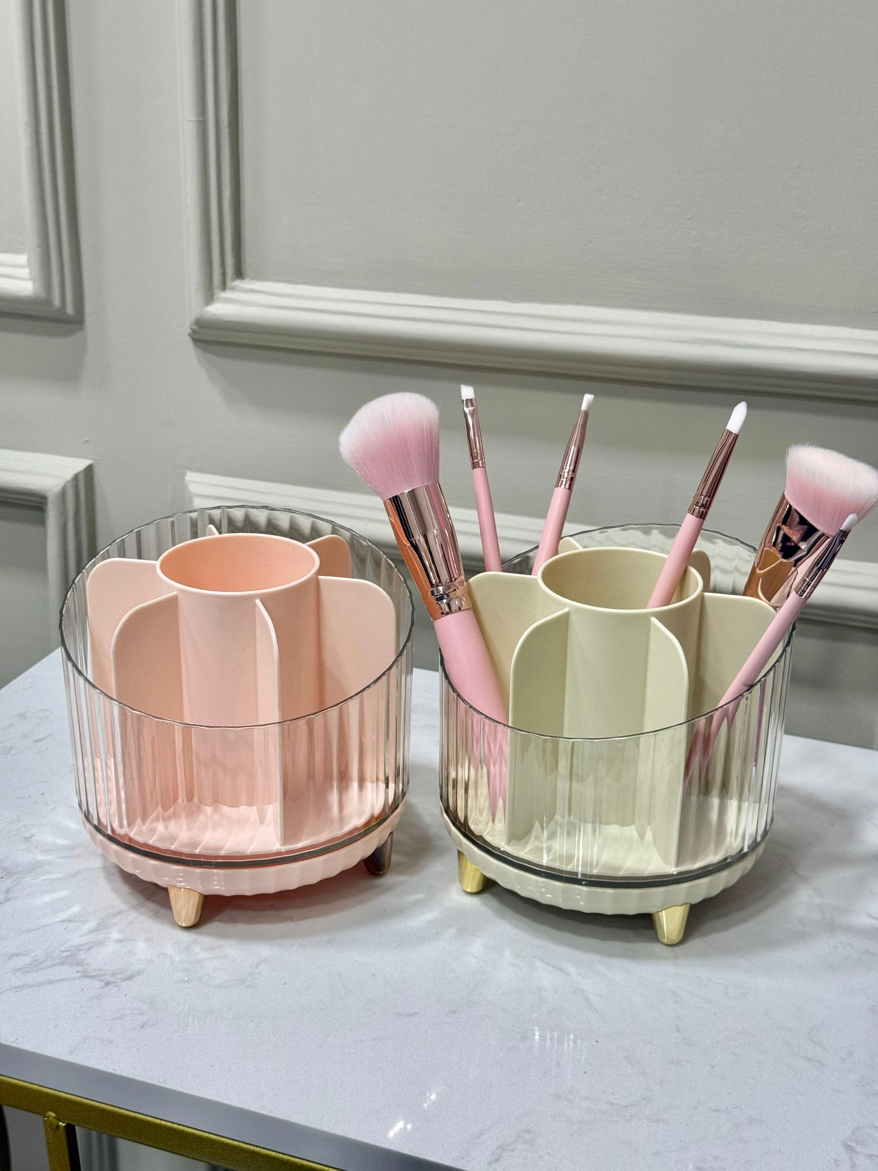 Organizador de brochas de maquillaje rosa y crema con compartimentos, patas doradas y acabado acanalado en cristal.