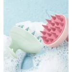 Cepillos masajeadores capilares, uno rosa y otro verde, con púas de silicona sobre espuma.