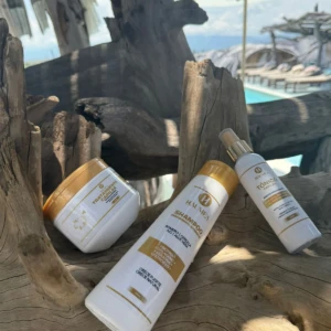 Combo capilar Haumea con tratamiento en tarro, shampoo de 400ml y tónico en spray, dispuestos sobre una madera clara en un entorno de piscina exterior.