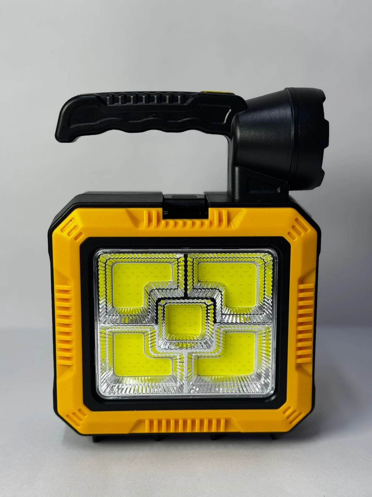 Linterna solar portátil amarilla y negra con manija plegable y múltiples paneles LED para camping y emergencias.