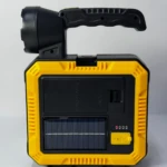 Linterna solar portátil amarilla y negra con asa, panel solar, puerto USB y luces indicadoras de carga.
