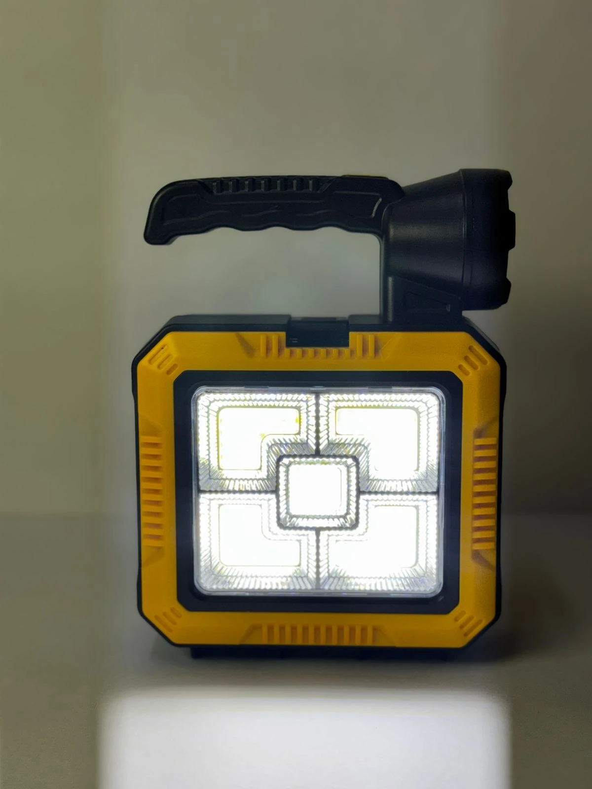 Lámpara solar portátil amarilla y negra con mango plegable y panel de luz LED frontal.