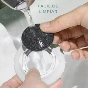 Pulidor de callos eléctrico, cabezal negro abrasivo mojándose bajo el grifo en lavamanos blanco. Texto: Fácil de limpiar.