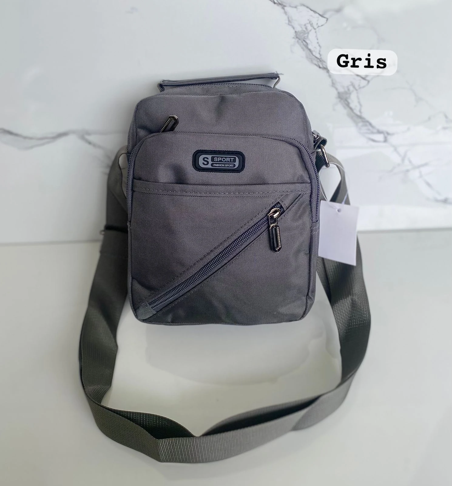 Carriel Sport color gris oscuro, tela texturizada, con logo "S SPORT" y correa ajustable, fondo mármol blanco.