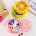 Pastilleros semanales frutales: naranja y pomelo, uno abierto con pastillas de colores.