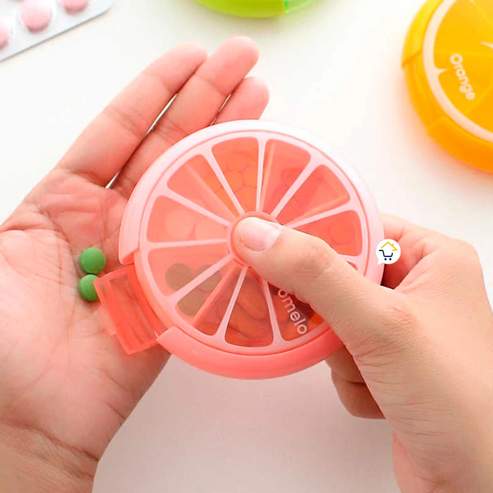 Pastillero semanal en forma de rodaja de pomelo rosa, con dos pastillas verdes al lado.