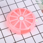 Pastillero semanal rosa con forma de pomelo, 7 compartimentos, tapa blanca central.