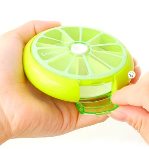 Pastillero semanal en forma de limón, con compartimentos transparentes y tapa abierta, sostenido en manos.