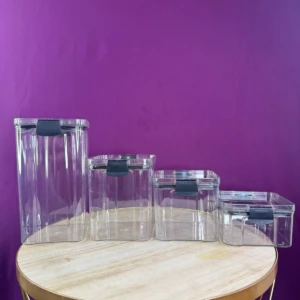 Organizador de cocina X4, recipientes rectangulares transparentes con tapas negras, apilables en mesa redonda.