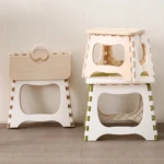 Tres taburetes plegables portátiles de plástico: uno cerrado color beige, dos apilados blancos con detalles en verde y beige.