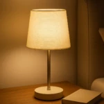 Lámpara de mesa recargable luz cálida, base redonda con botón de encendido, sobre mesa de noche junto a un libro.