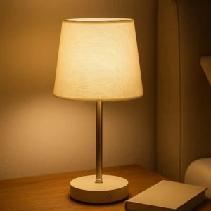 Lámpara de mesa recargable luz cálida, base redonda con botón de encendido, sobre mesa de noche junto a un libro.