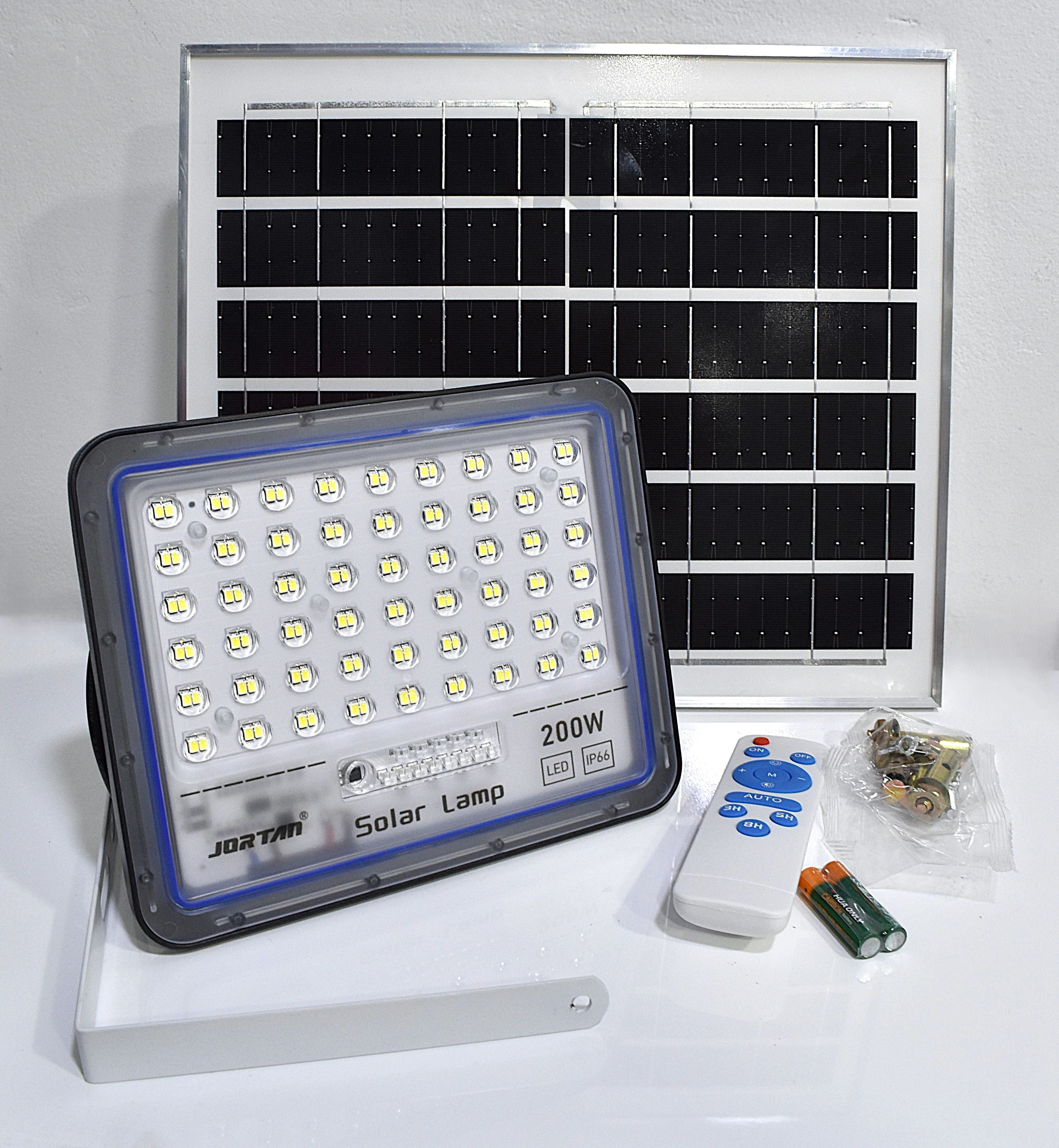 Lámpara solar Jortan 200W con panel rectangular, reflector LED, control remoto, baterías y kit de montaje metálico dispuestos sobre superficie blanca.