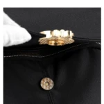 Bolso negro con broche magnético dorado y detalle de cierre visible.