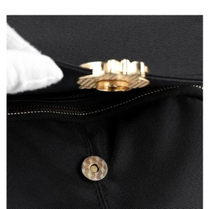 Bolso negro con broche magnético dorado y detalle de cierre visible.